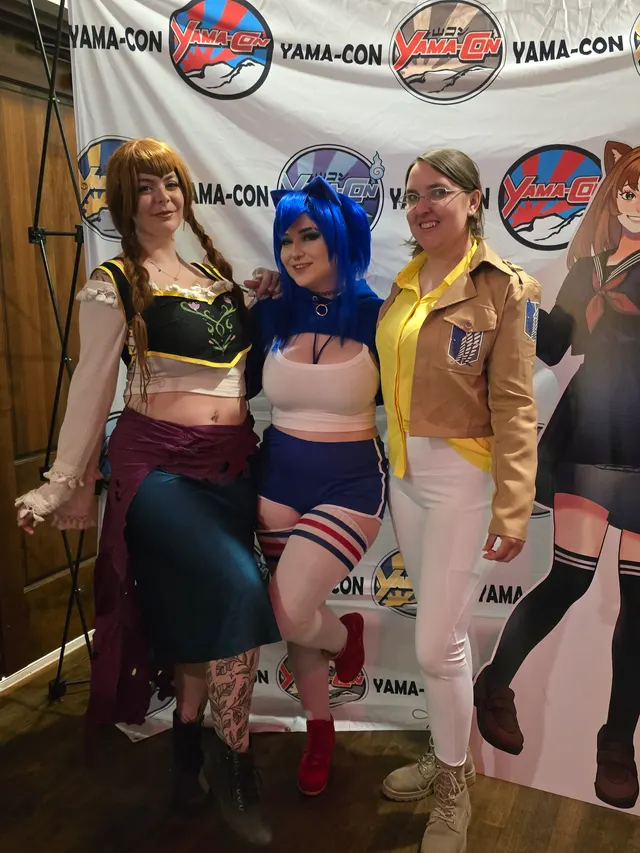 three cosplayers posing at a photo backdrop