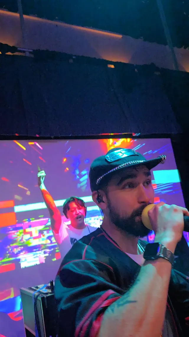 MC on mic with hype man and DJ booth under club lighting
